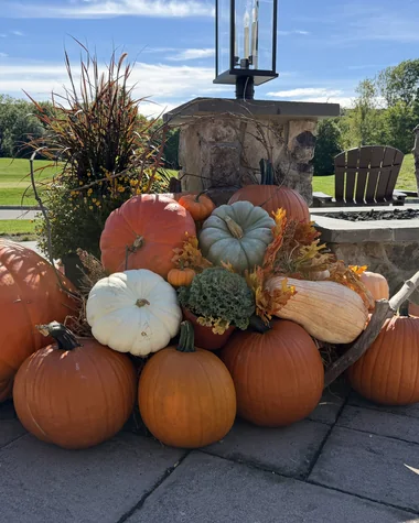 Large pumpkins and gourds stacked at the base of a stone pillar, with the course beyond