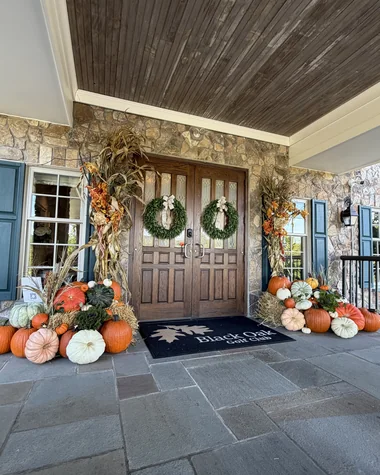Double wood doors with wreaths, flanked by pumpkin arrangements under a covered entry