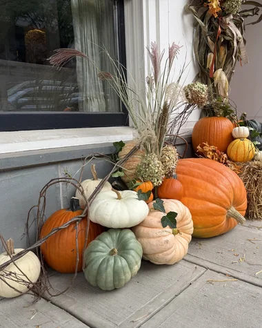 Pumpkins, gourds and hay bales along a storefront, with cornstalk arrangements at the columns