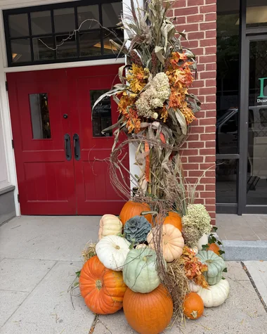 A cornstalk column with pumpkins at its base beside a red double door