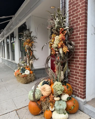 A brick storefront corner with a cornstalk arrangement and pumpkins on hay