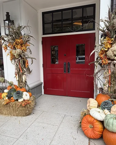 A red door framed by two cornstalk arrangements, pumpkins and hay at each side