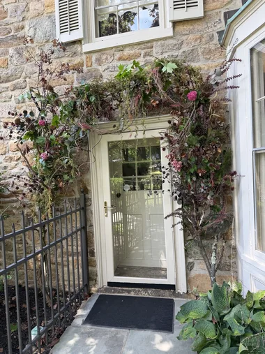 A stone farmhouse doorway framed by a built floral arch in autumn tones