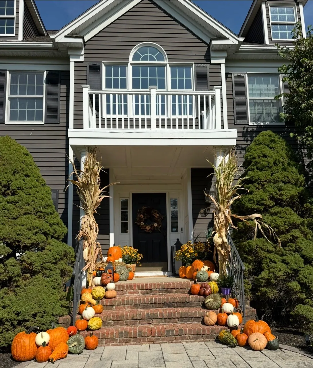 A colonial entry with cornstalks and pumpkins running the full width of the brick steps